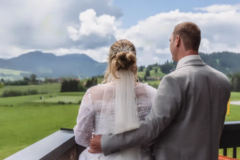 Brautpaar blickt von einer Terrasse auf das Bergpanorama im Allgäu