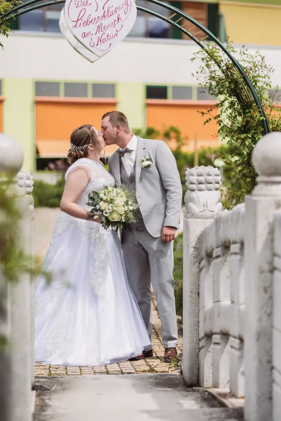 Romantischer Hochzeitskuss unter Blütenbogen - Hochzeitsfotografie Allgäu